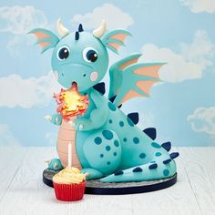 a blue dragon figurine sitting next to a cupcake with a candle in it