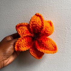 an orange crocheted flower being held by someone's hand on a white wall