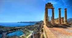 an ancient greek temple overlooks the sea and mountains on a sunny day with blue skies