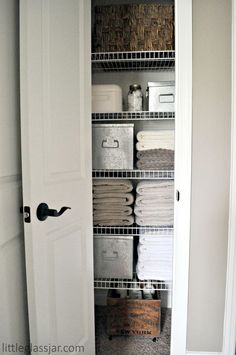 an organized closet with baskets and linens on the shelves, in front of a white door