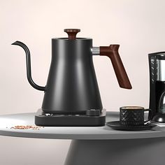 a black coffee pot sitting on top of a table next to a cup of coffee