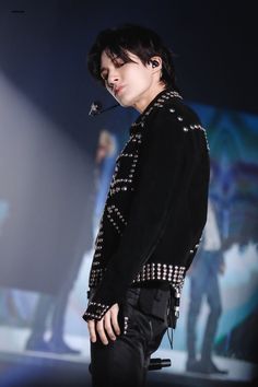 a man with black hair and piercings standing in front of a stage holding a microphone