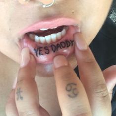 a person with tattoos on their fingers holding up the word yes daddy in front of her mouth