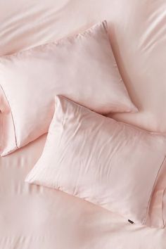 two pink pillows sitting on top of a bed next to sheets and pillowcases