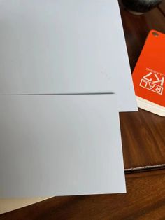 an orange and white book sitting on top of a wooden table next to a computer mouse