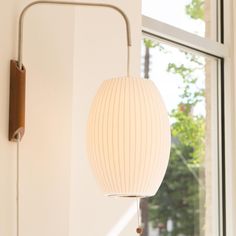 a white light hanging from the side of a wall next to a window with a lamp on it