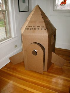 a cardboard birdhouse sitting on top of a hard wood floor next to a window