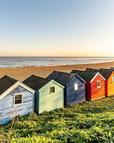 colorful beach huts line the grass near the water's edge in front of an ocean