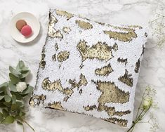 a white and gold sequin pillow sitting on top of a table next to flowers