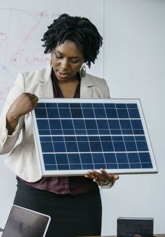 a woman holding up a solar panel in front of her laptop computer on a desk