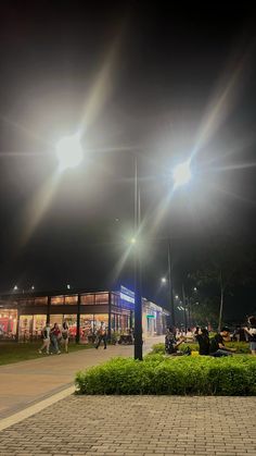 people are sitting on benches in the park at night with bright lights shining over them