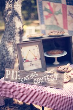 a table topped with pies next to a wooden sign that says pie eating contest