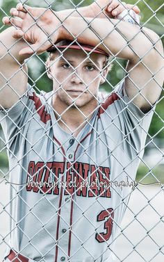 a baseball player is holding his head behind a chain link fence and posing for the camera