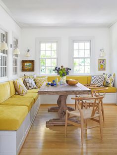 a yellow couch and table in a room with white walls, wood floors and windows