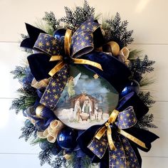 a christmas wreath with a nativity scene on it and gold ribbons hanging from the front