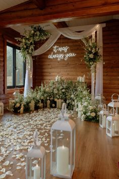 a wedding ceremony with white flowers and candles on the floor in front of a wooden wall that says it was always you