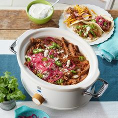 two tacos in a crock pot on top of a table with plates and utensils