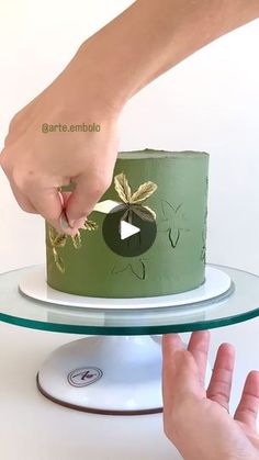 someone is decorating a green cake on a glass platter with gold leaf decorations