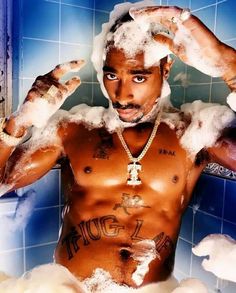 a shirtless man is in the shower with foam on his head and hands above his head