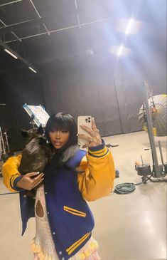 a woman taking a selfie with her cell phone in an empty warehouse area while wearing a blue and yellow jacket