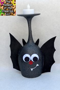 a black candle holder with a bat on it's side and a white candle in the middle