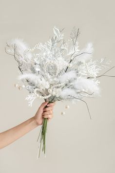 a person holding a bouquet of white flowers and feathers in their hand, on a gray background