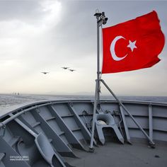 there is a flag on the back of a boat with birds flying in the background