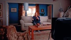 a woman sitting on top of a couch in a living room next to a tv