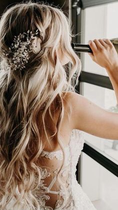 a woman in a wedding dress looking out the window with her hair comb in her hand