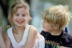 two young children sitting next to each other on a park bench smiling at each other