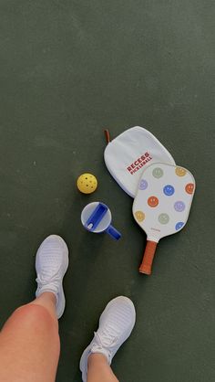 a child's foot next to a toy tennis racket and ball