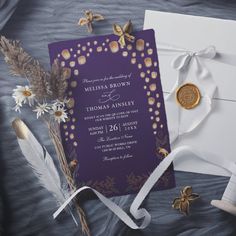 a purple and gold wedding card on top of a white envelope next to some flowers