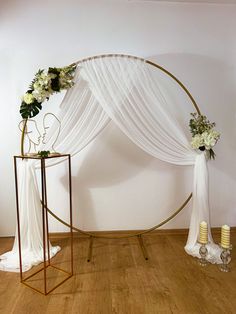 an arch decorated with white flowers and greenery sits in the center of a wood floored room