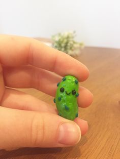 a hand holding a tiny green object on top of a wooden table