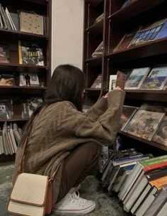 a woman sitting on the floor in front of a bookshelf holding up a book