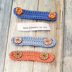 three crocheted hair clips with buttons on them sitting on a wooden floor next to a sign that says mask extenders for you