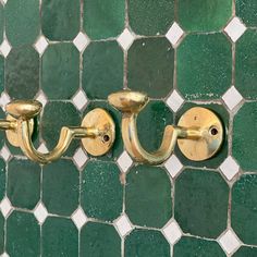 two brass hooks on a green tiled wall