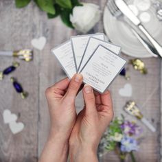 a person holding four cards in their hands with flowers on the table and other decorations around them