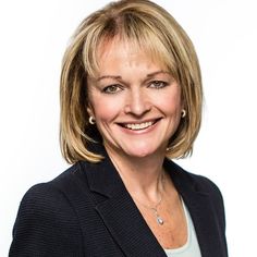 a woman with blonde hair wearing a black jacket and smiling at the camera while standing in front of a white background