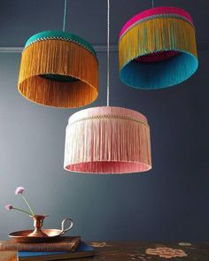 three colorful lamps hanging from the ceiling above a table with a book and vase on it