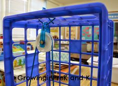 a blue cage with a white object hanging from it's side in a classroom