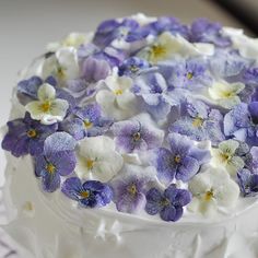 a white cake with purple and white flowers on it's icing, sitting on a plate