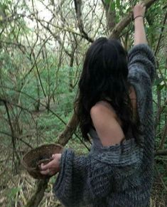 a woman in the woods reaching up to grab something out of a bowl that she is holding