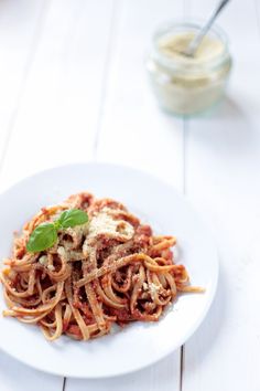 a white plate topped with pasta and sauce on top of a wooden table next to a jar of dressing