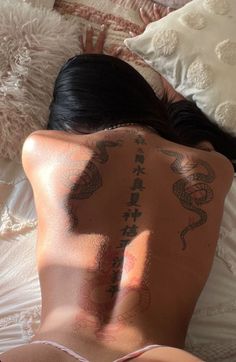 a woman laying on top of a bed with tattoos on her back and arms behind her head