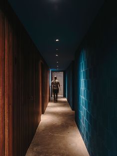 a man walking down a long hallway with blue walls and wooden doors on both sides