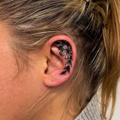 a woman's ear is decorated with black ink and has a flower tattoo on it