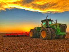 a tractor is parked in the middle of a field as the sun sets behind it