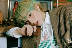 a young man with green hair is leaning on a desk and looking at the camera