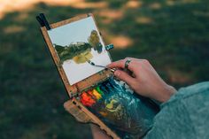 a person is holding an easel and painting with watercolors on the canvas